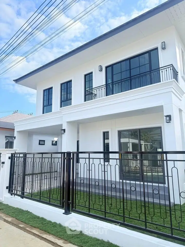 Modern two-story white house with sleek black railings and large windows, showcasing contemporary architecture.