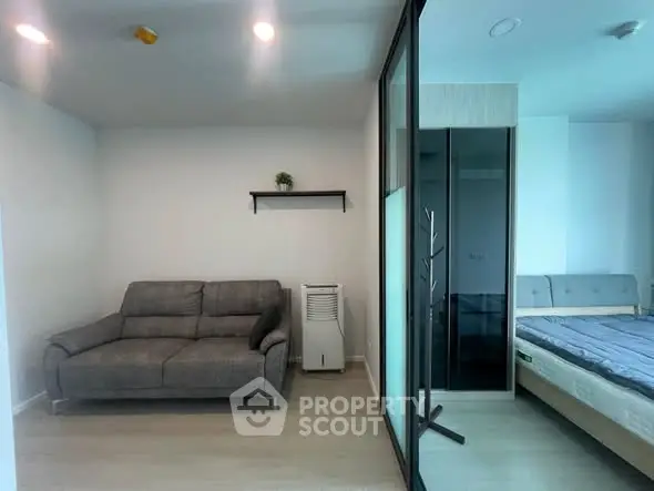 Modern apartment interior with cozy living room and stylish bedroom separated by glass partition.