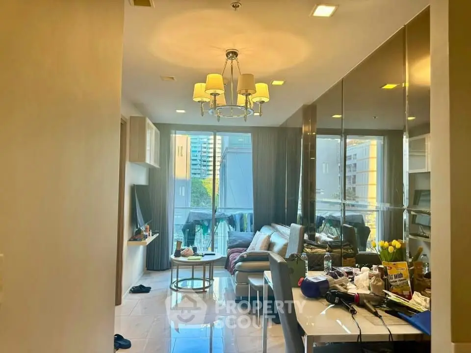 Modern living room with elegant chandelier and city view, featuring sleek furniture and reflective surfaces.