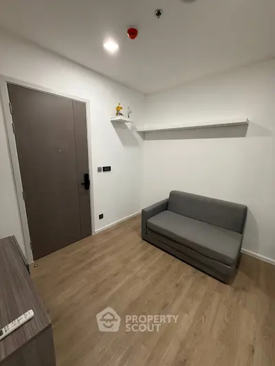 Cozy small living room with modern decor and wooden flooring, featuring a compact gray sofa and minimalist shelving.