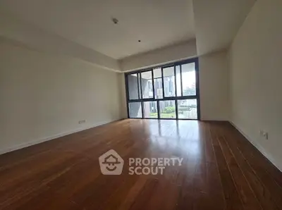Spacious empty room with wooden flooring and large windows offering natural light.