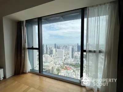 Spacious high-rise living room with floor-to-ceiling windows offering a panoramic city view, hardwood floors, and sheer curtains.