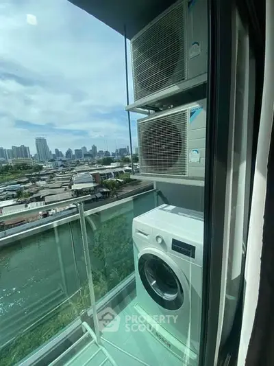 Compact balcony with washing machine and air conditioning units overlooking cityscape.
