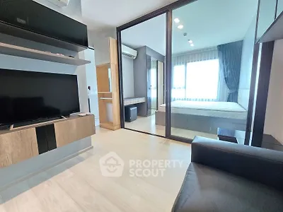 Modern apartment interior with sleek living room and cozy bedroom separated by glass partition.