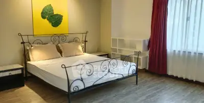 Spacious bedroom with elegant metal bed frame and large window with red curtains.