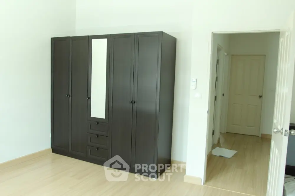 Spacious bedroom with elegant dark wardrobe and light wooden flooring