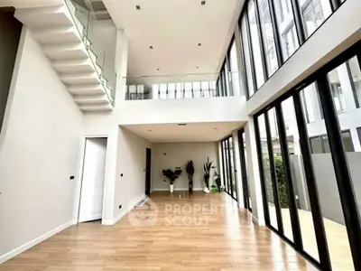 Spacious modern living room with high ceilings and large windows, featuring elegant wooden flooring and a mezzanine.