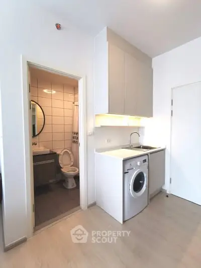 Compact apartment interior with modern kitchen and bathroom, featuring washing machine and sleek cabinetry.
