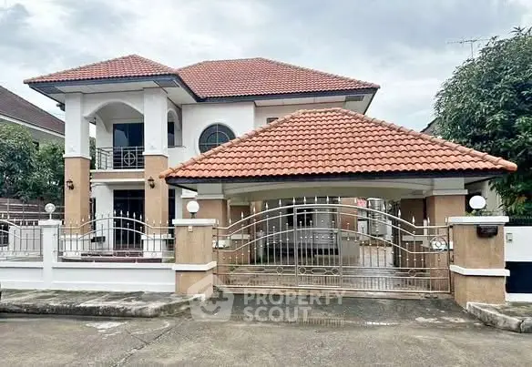 Charming two-story house with red-tiled roof and gated entrance in a serene neighborhood.