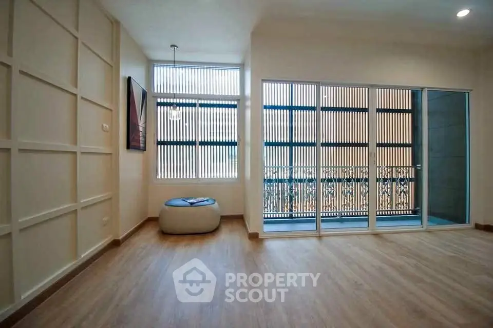 Spacious living room with large windows and balcony access, featuring modern wooden flooring.