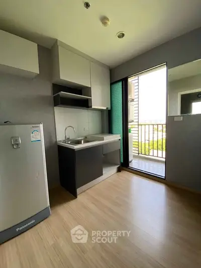 Modern compact kitchen with balcony access and sleek appliances in urban apartment.