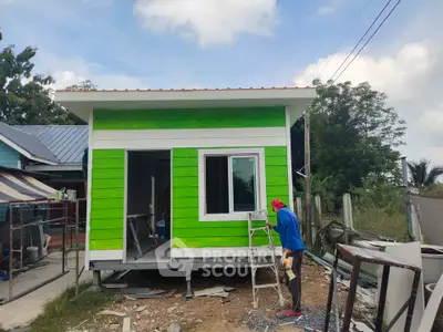 Charming small green house under construction with worker painting exterior