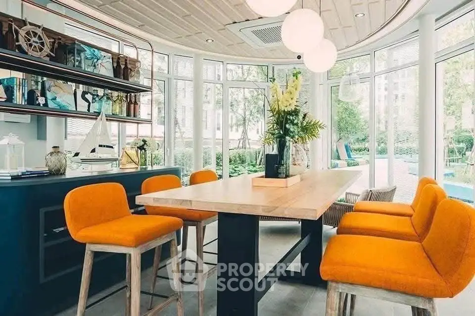 Modern dining area with vibrant orange chairs and large windows overlooking greenery.