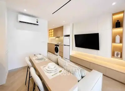Modern open-plan living room with dining area, sleek kitchen, and wall-mounted TV in a stylish apartment.