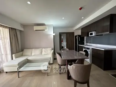 Modern open-layout living room with kitchen, featuring sleek furniture and natural light.