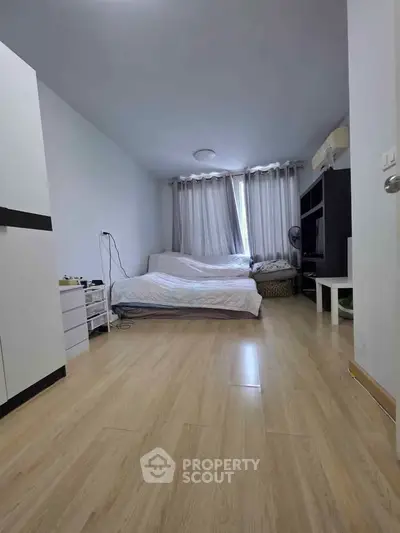 Spacious bedroom with wooden flooring and natural light, featuring a cozy bed and modern furnishings.