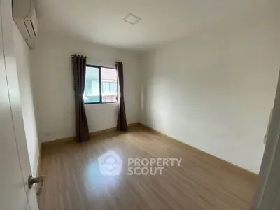 Spacious empty bedroom with wooden flooring and natural light from window.