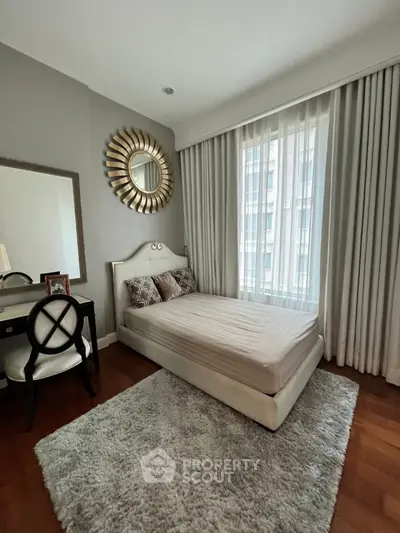 Elegant bedroom with stylish decor and large window, featuring a cozy bed and chic mirror.