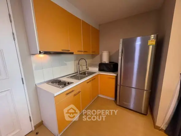 Compact modern kitchen with vibrant orange cabinets and stainless steel fridge