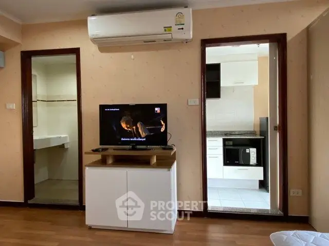 Cozy living room with air conditioning and TV, adjacent to a modern kitchen with appliances.