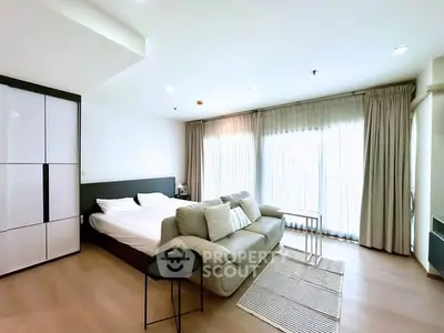 Spacious modern bedroom with cozy seating area and large windows for natural light.