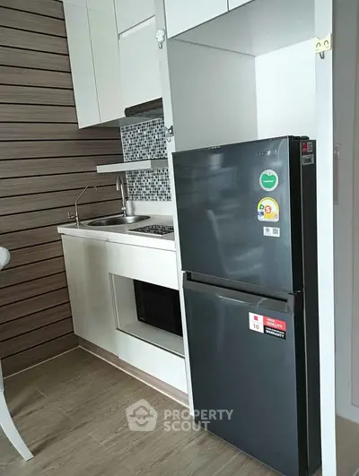 Modern compact kitchen with sleek black fridge and built-in oven in stylish apartment.