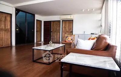 Spacious living room with modern furniture and wooden accents, featuring large windows for natural light.