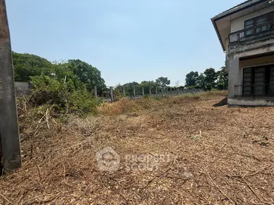 Spacious land plot with potential for development, featuring a partially visible building and lush greenery.