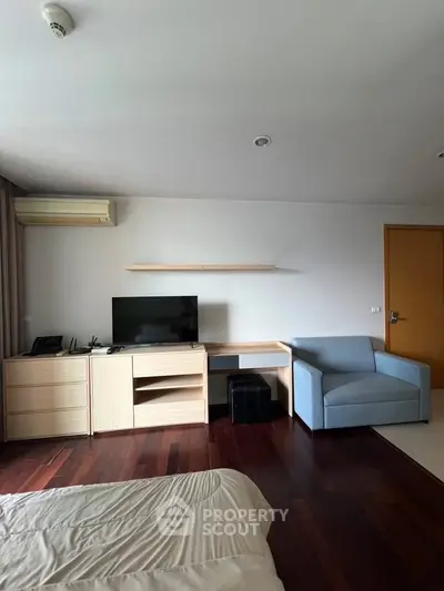 Modern bedroom with wooden flooring, TV, and cozy seating area.