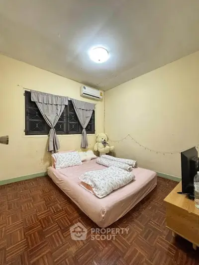 Cozy bedroom with parquet flooring, soft pink bedding, and a large teddy bear for a welcoming atmosphere.