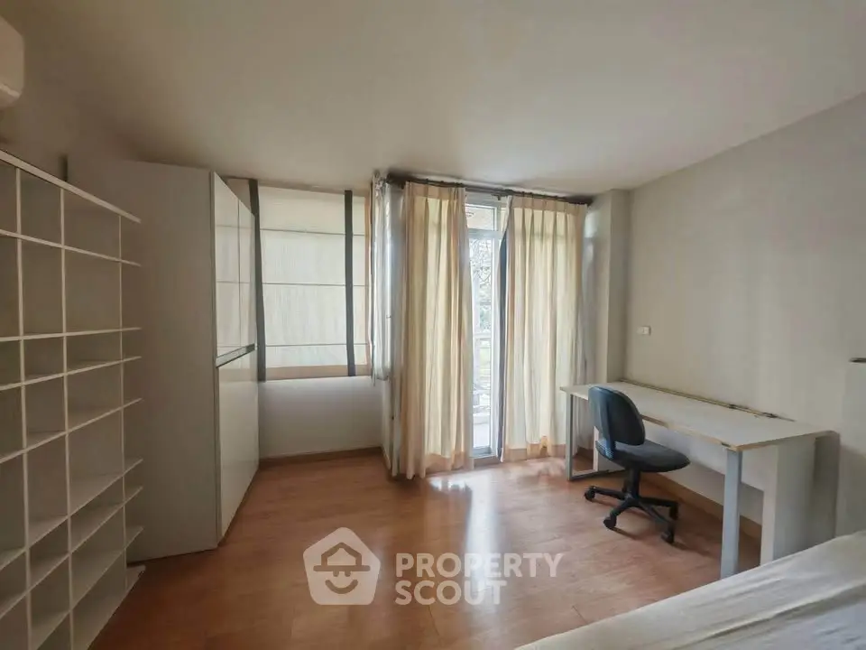 Spacious bedroom with natural light, wooden flooring, and study desk near window.