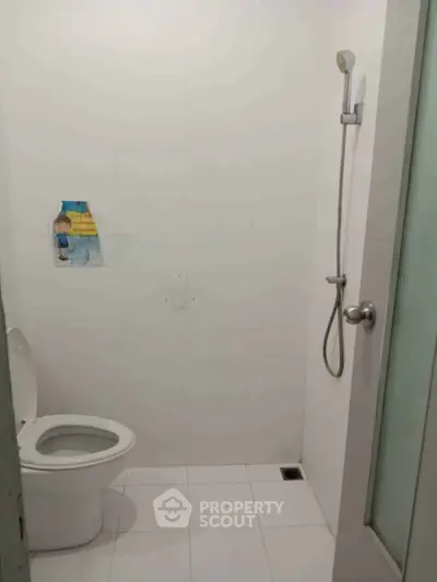 Minimalist bathroom with shower and toilet in a clean white tiled space.