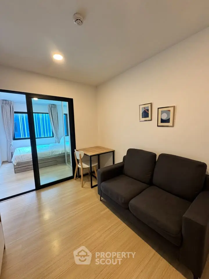 Modern living room with cozy sofa and view into a stylish bedroom through glass doors.