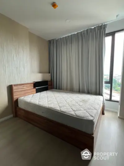 Spacious bedroom with large window and modern wooden bed frame in a high-rise apartment.