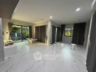 Spacious modern living room with marble flooring and large windows overlooking a lush garden.