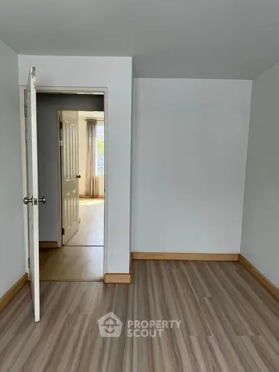 Spacious empty room with wooden flooring and open door leading to bright area.