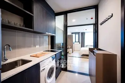 Modern apartment kitchen with washing machine and open layout to bedroom.