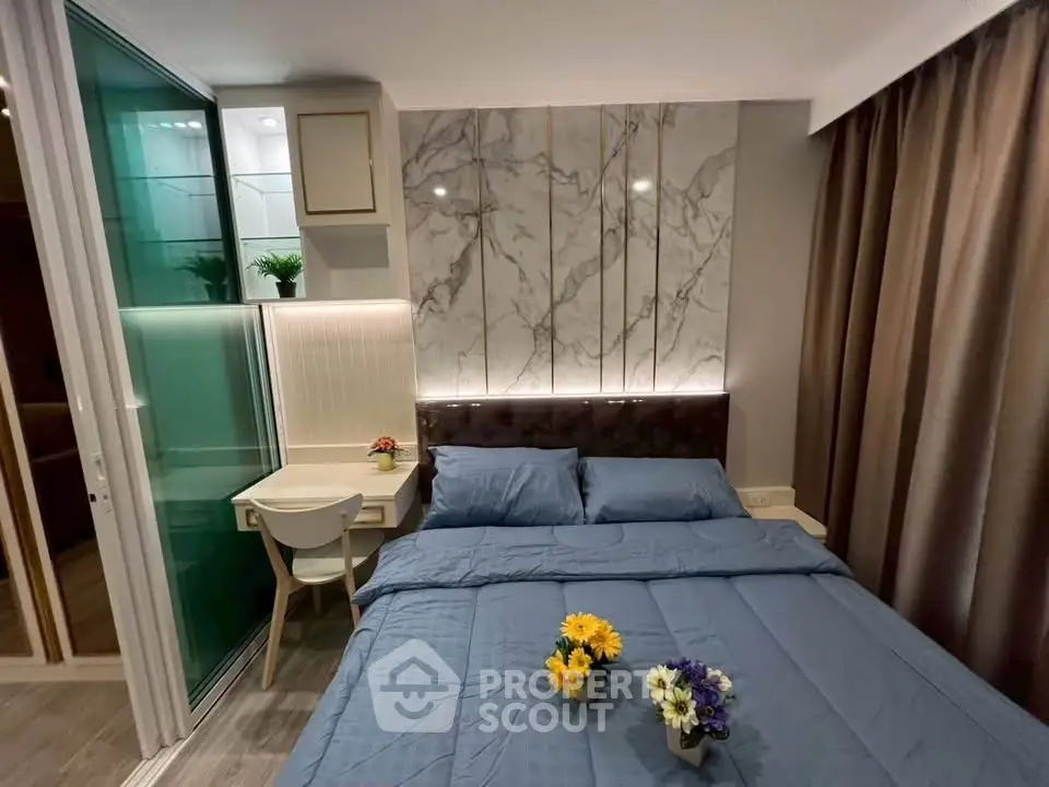 Modern bedroom with elegant marble accent wall and cozy blue bedding, featuring a compact study nook.
