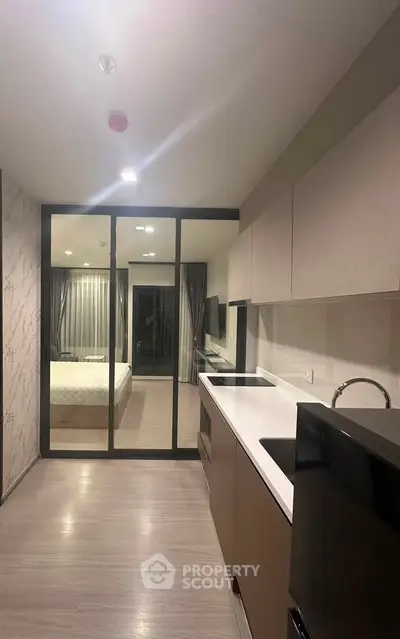 Modern open-layout kitchen with sleek cabinetry and view into a stylish bedroom through glass partition.