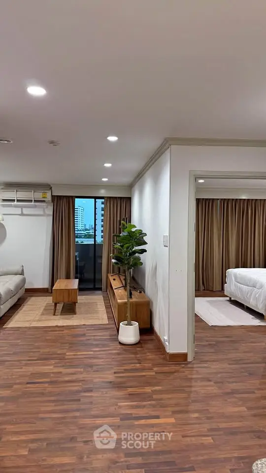 Spacious open-plan living room with modern decor and wooden flooring, featuring a cozy bedroom view.