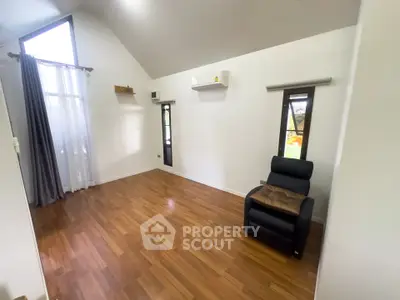 Spacious living room with high ceiling and wooden flooring, featuring a cozy armchair and large windows.