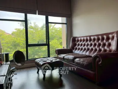 Cozy living room with leather sofa and large window offering lush green views.