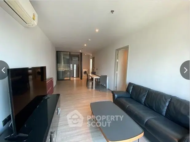 Spacious living room with sleek hardwood floors, modern furniture, and an open-plan kitchen, bathed in natural light from large windows.