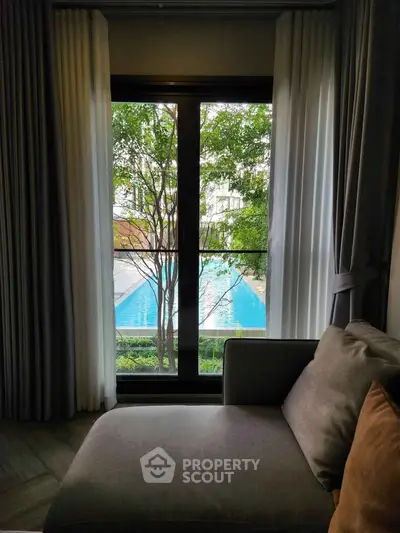 Luxurious living room with pool view through large window, featuring elegant curtains and cozy seating.