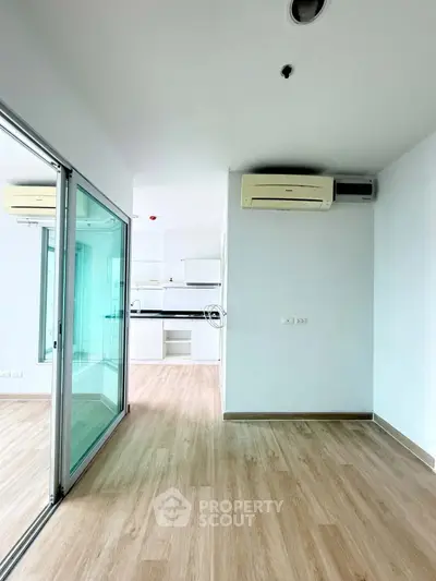 Modern apartment interior with open layout and wooden flooring, featuring a sleek kitchen and air conditioning.