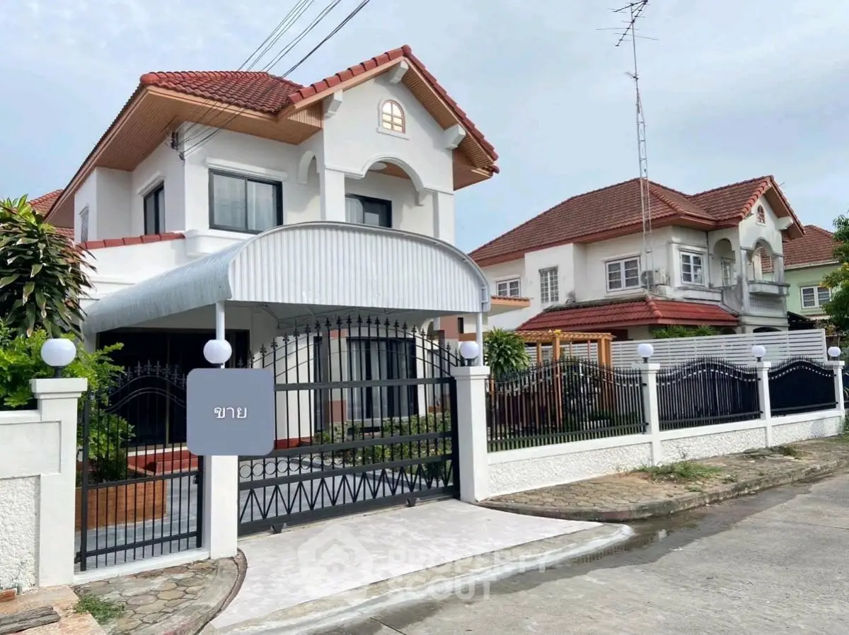 Charming two-story house with red-tiled roof and gated entrance in a serene neighborhood.