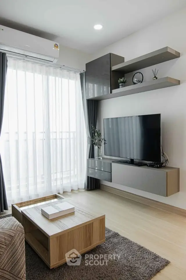 Modern living room with sleek furniture and large TV, featuring natural light from floor-to-ceiling windows.