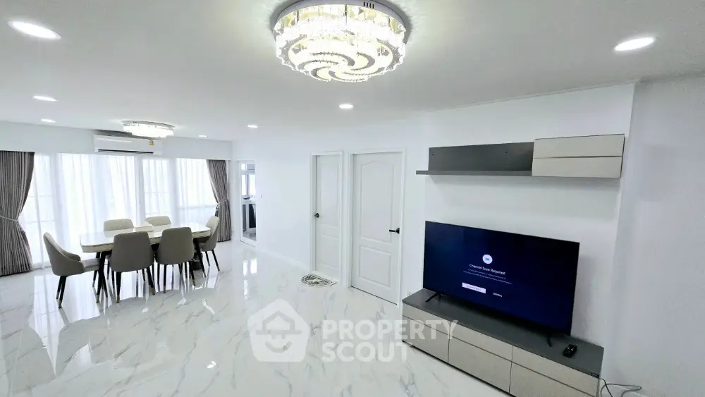Spacious modern living room with elegant chandelier and dining area, featuring sleek marble flooring.