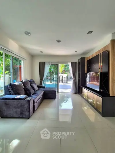 Spacious living room with modern sofa and entertainment unit, featuring large windows and garden view.