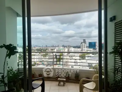 Stunning cityscape view from a high-rise balcony with lush potted plants and cozy seating.
